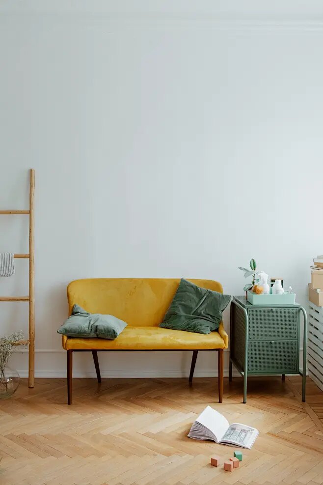 A bright, calm room with a soft yellow sofa, warm wood floor and trailing green plant